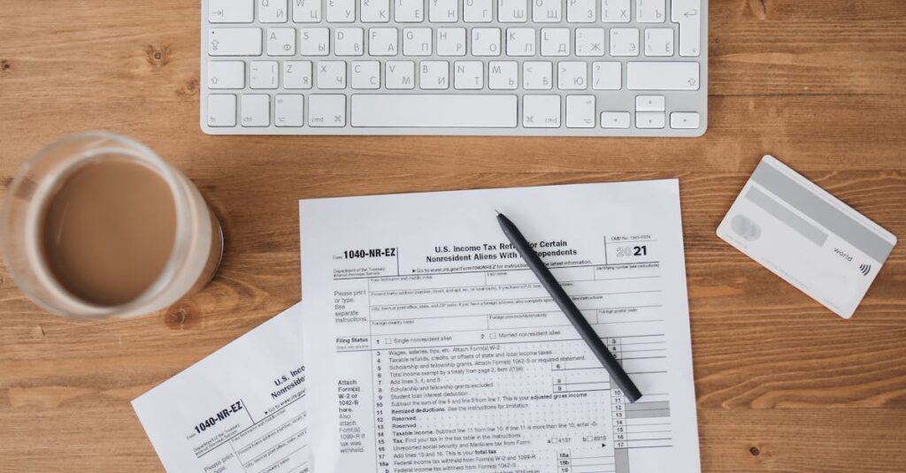 Top view of tax forms, keyboard, pen, and coffee on a wooden desk.